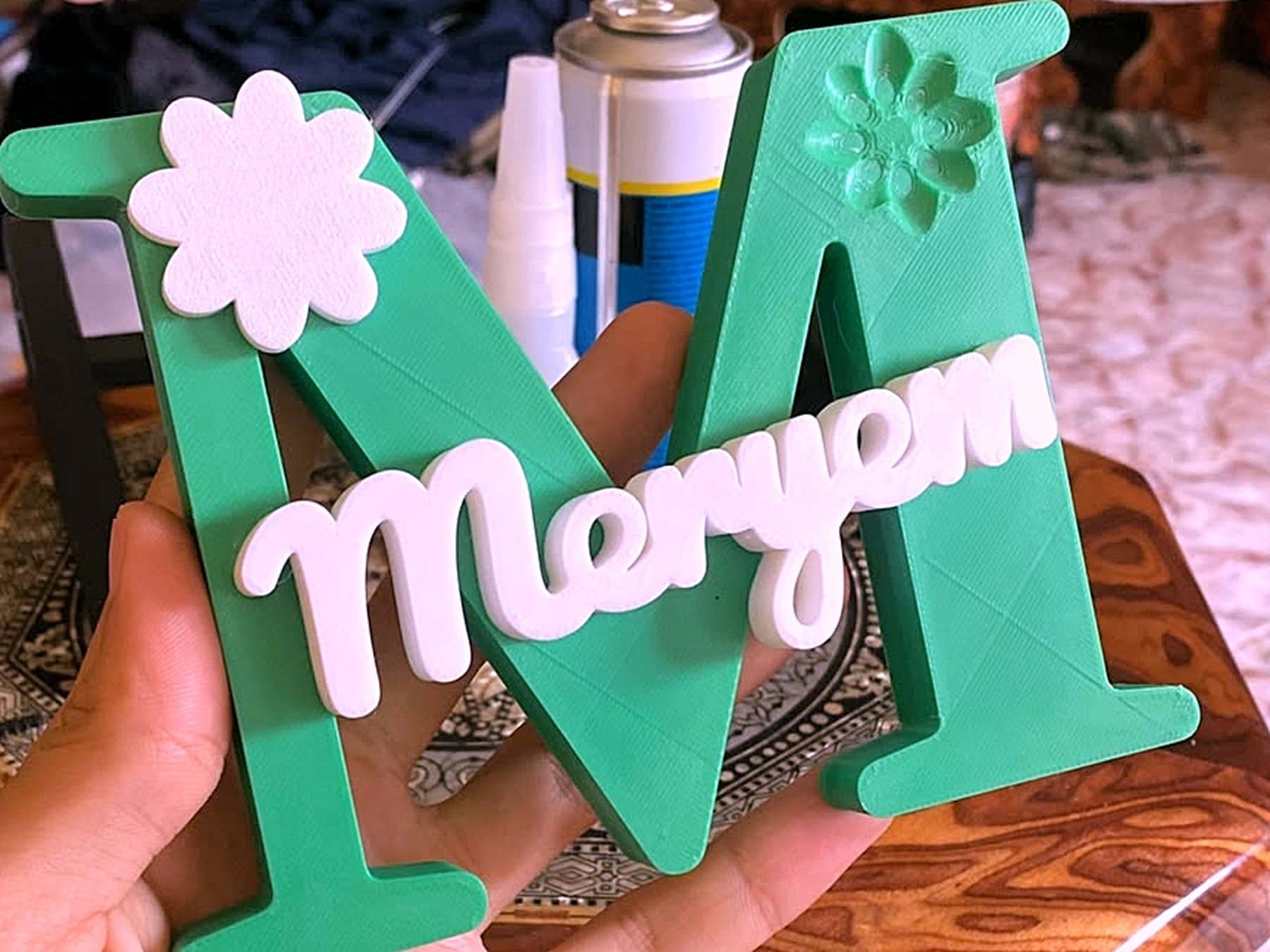 Monogramme vert au prénom Meryem tenu en main devant l'établi