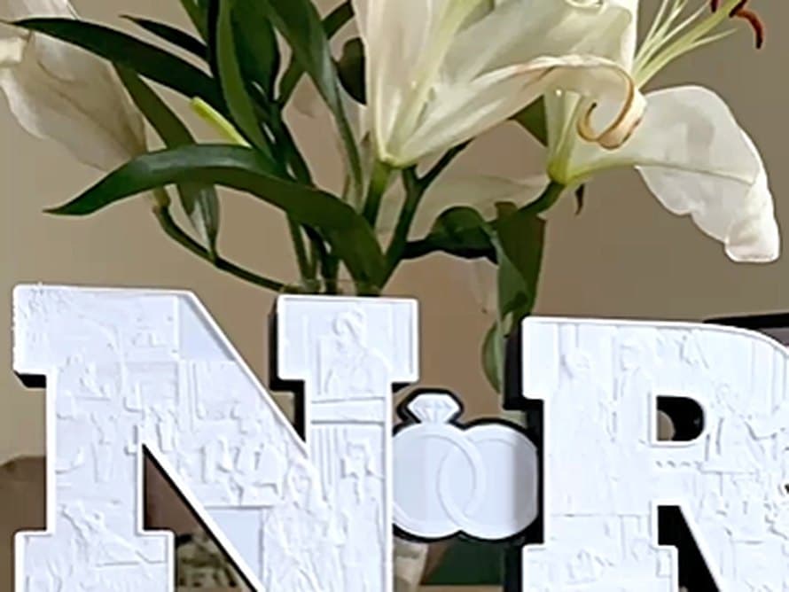 Monogramme de mariage aux initiales N et R, posé devant un bouquet de lys blancs